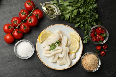 Photo of Raw squid rings, parsley, lemon, other products and spices on dark textured table, flat lay