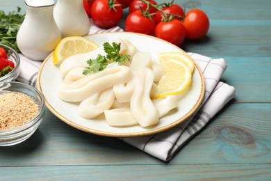 Photo of Raw squid rings, parsley, lemon, spices and tomatoes on light blue wooden table, closeup