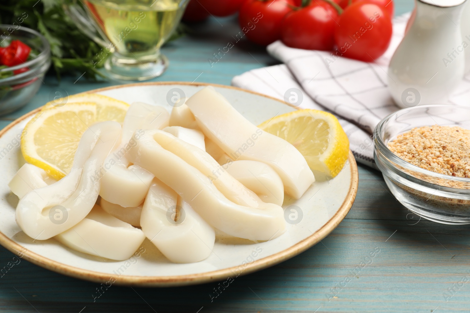 Photo of Raw squid rings, lemon and spices on light blue wooden table, closeup