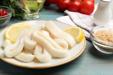 Photo of Raw squid rings, lemon and spices on light blue wooden table, closeup