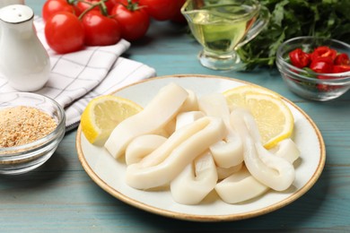 Photo of Raw squid rings, lemon and spices on light blue wooden table, closeup