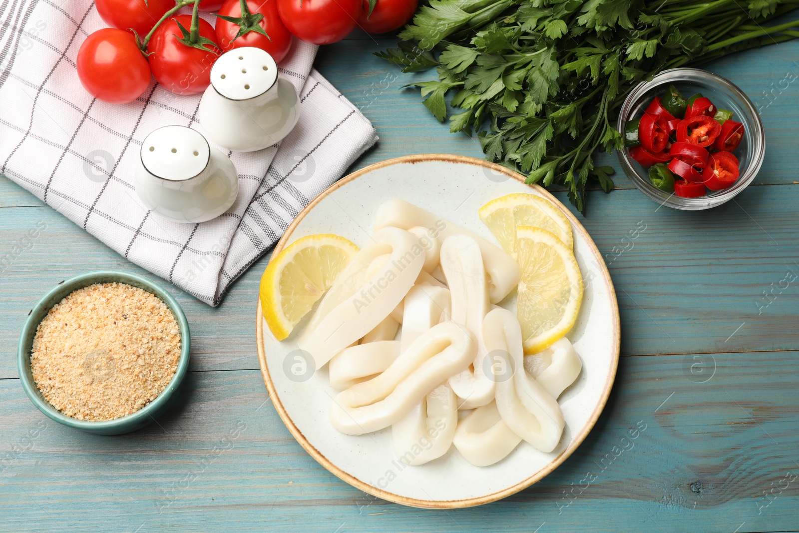 Photo of Raw squid rings, lemon, parsley, spices and tomatoes on light blue wooden table, flat lay