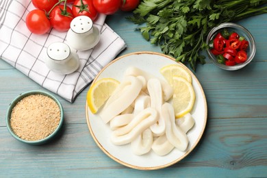 Photo of Raw squid rings, lemon, parsley, spices and tomatoes on light blue wooden table, flat lay