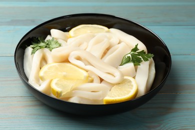 Photo of Raw squid rings, parsley and lemon in bowl on light blue wooden table, closeup