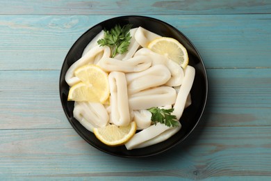Photo of Raw squid rings, parsley and lemon in bowl on light blue wooden table, top view