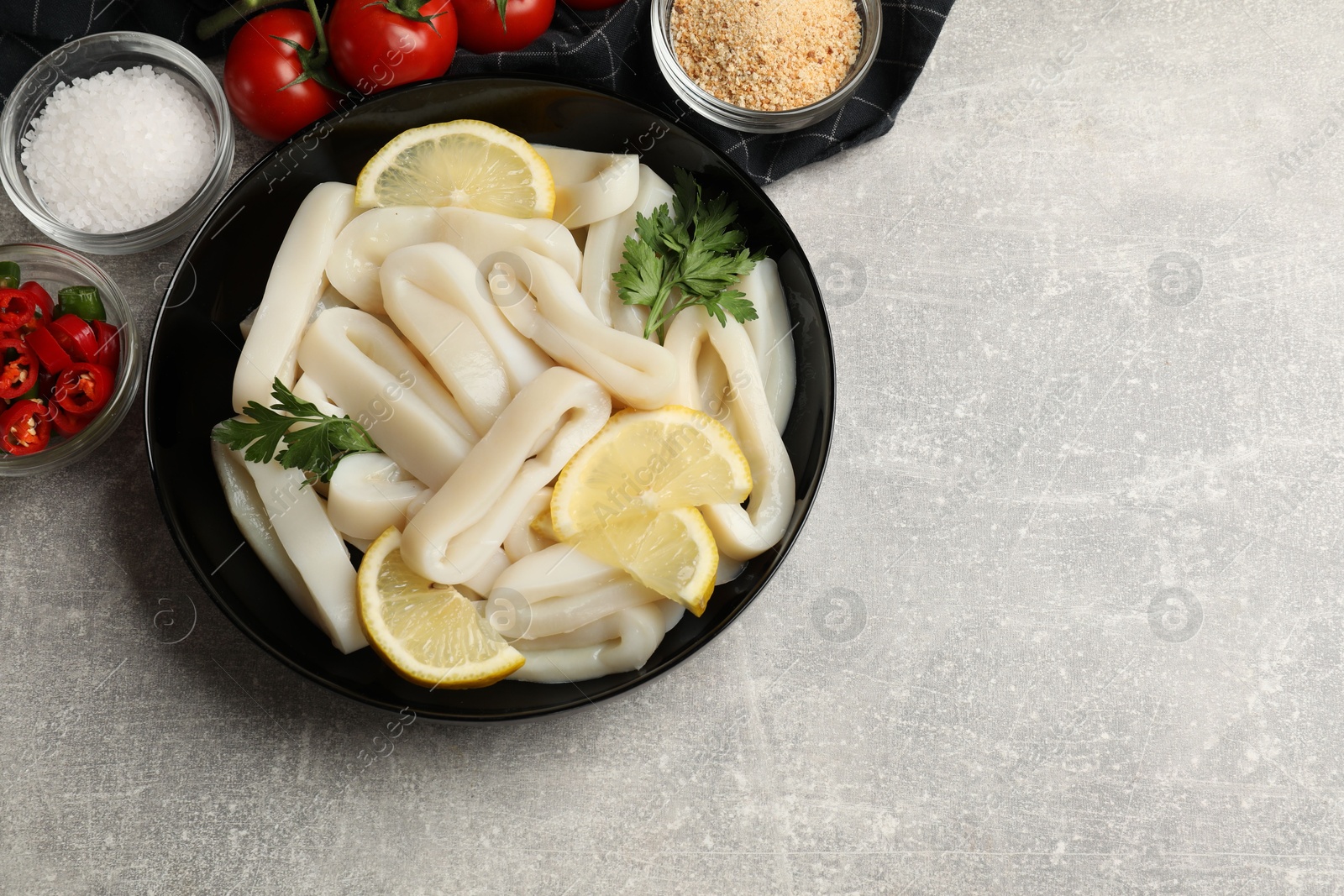 Photo of Raw squid rings, lemon, parsley, spices and products on grey textured table, flat lay. Space for text