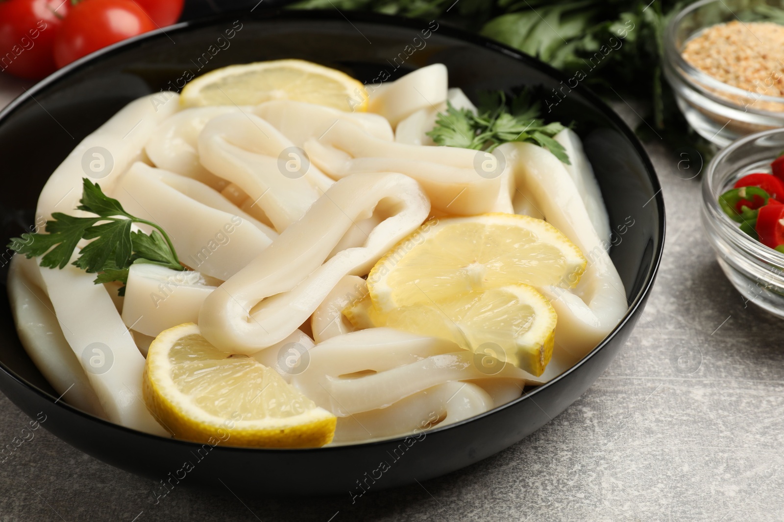 Photo of Raw squid rings, lemon and parsley on grey textured table, closeup