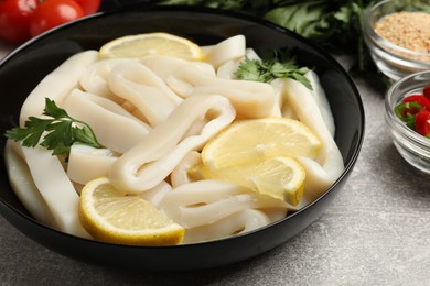 Photo of Raw squid rings, lemon and parsley on grey textured table, closeup