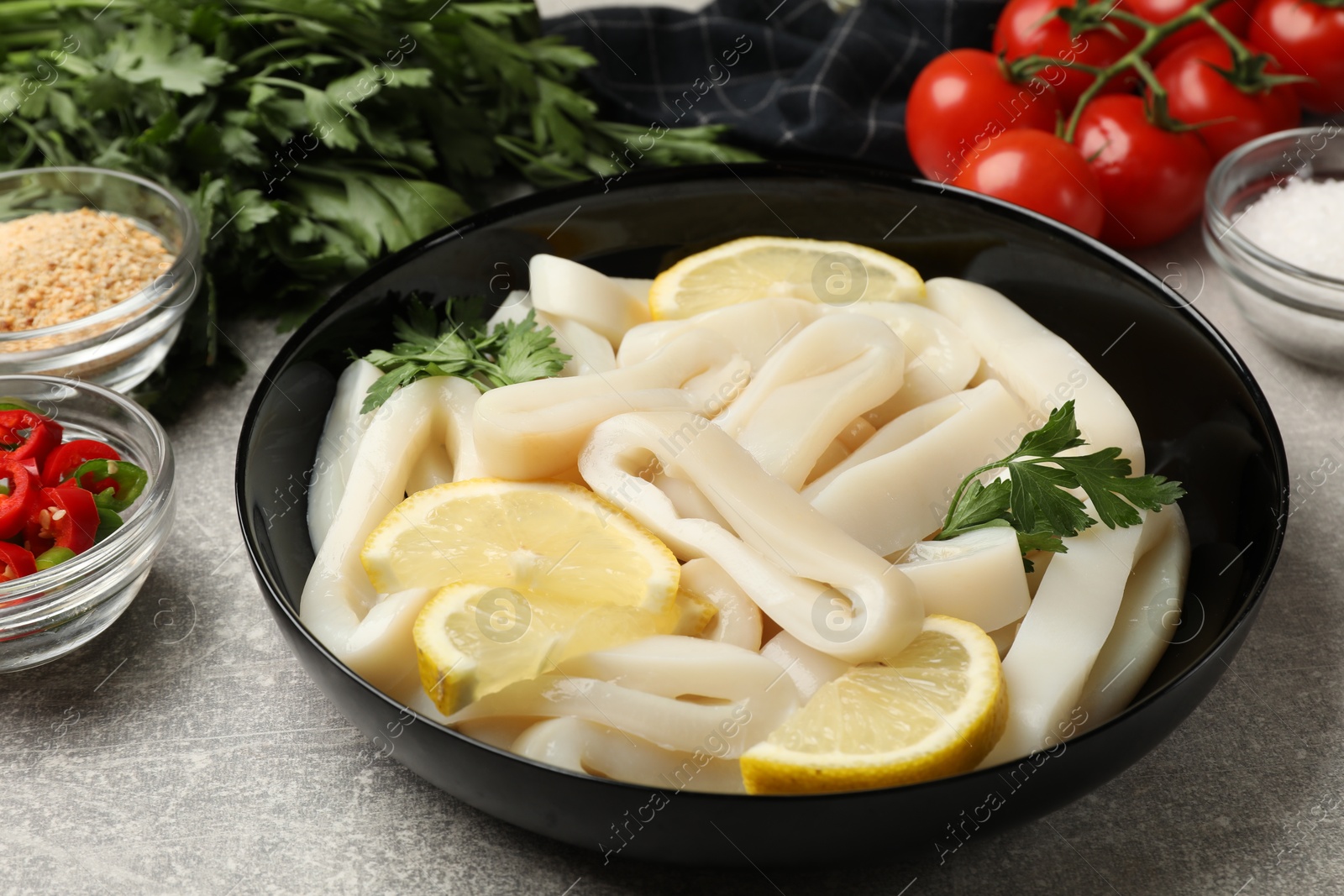 Photo of Raw squid rings, lemon, parsley, spices and products on grey textured table, closeup