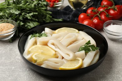 Photo of Raw squid rings, lemon, parsley, spices and products on grey textured table, closeup