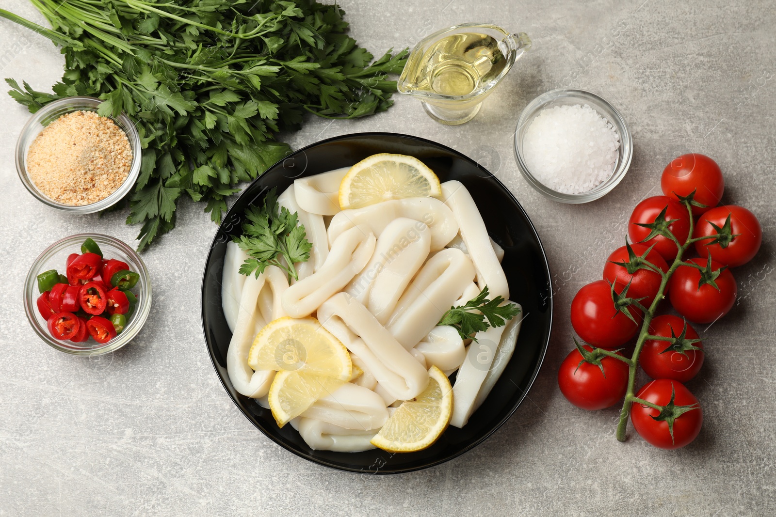 Photo of Raw squid rings, lemon, parsley, spices and products on grey textured table, flat lay