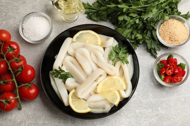 Photo of Raw squid rings, lemon, parsley, spices and products on grey textured table, flat lay