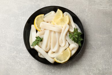 Photo of Raw squid rings, lemon and parsley in bowl on grey textured table, top view