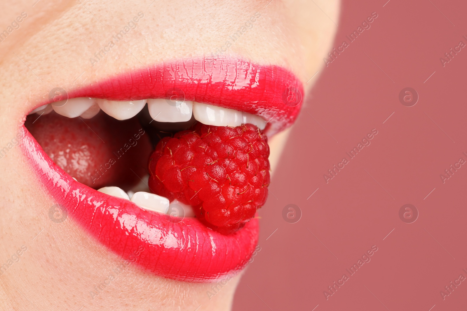 Photo of Woman with beautiful lips makeup and raspberry on dusty pink background, closeup. Space for text