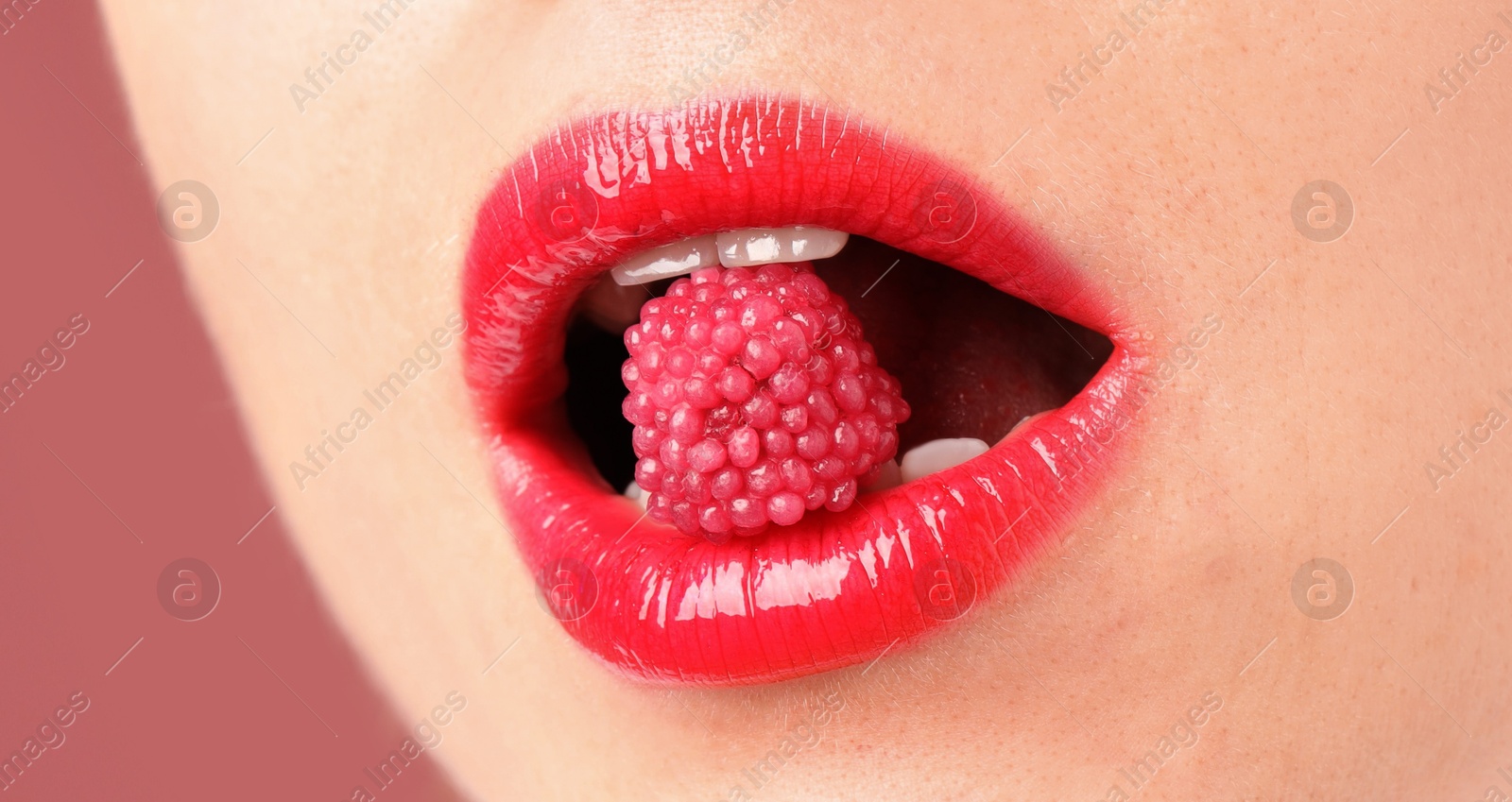 Photo of Woman with beautiful lips makeup and raspberry candy on dusty pink background, closeup