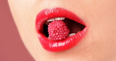 Photo of Woman with beautiful lips makeup and raspberry candy on dusty pink background, closeup