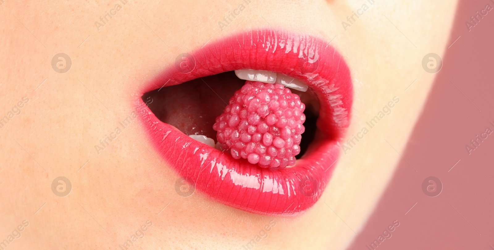 Photo of Woman with beautiful lips makeup and raspberry candy on dusty pink background, closeup