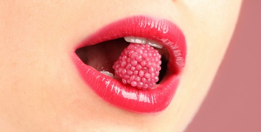 Photo of Woman with beautiful lips makeup and raspberry candy on dusty pink background, closeup