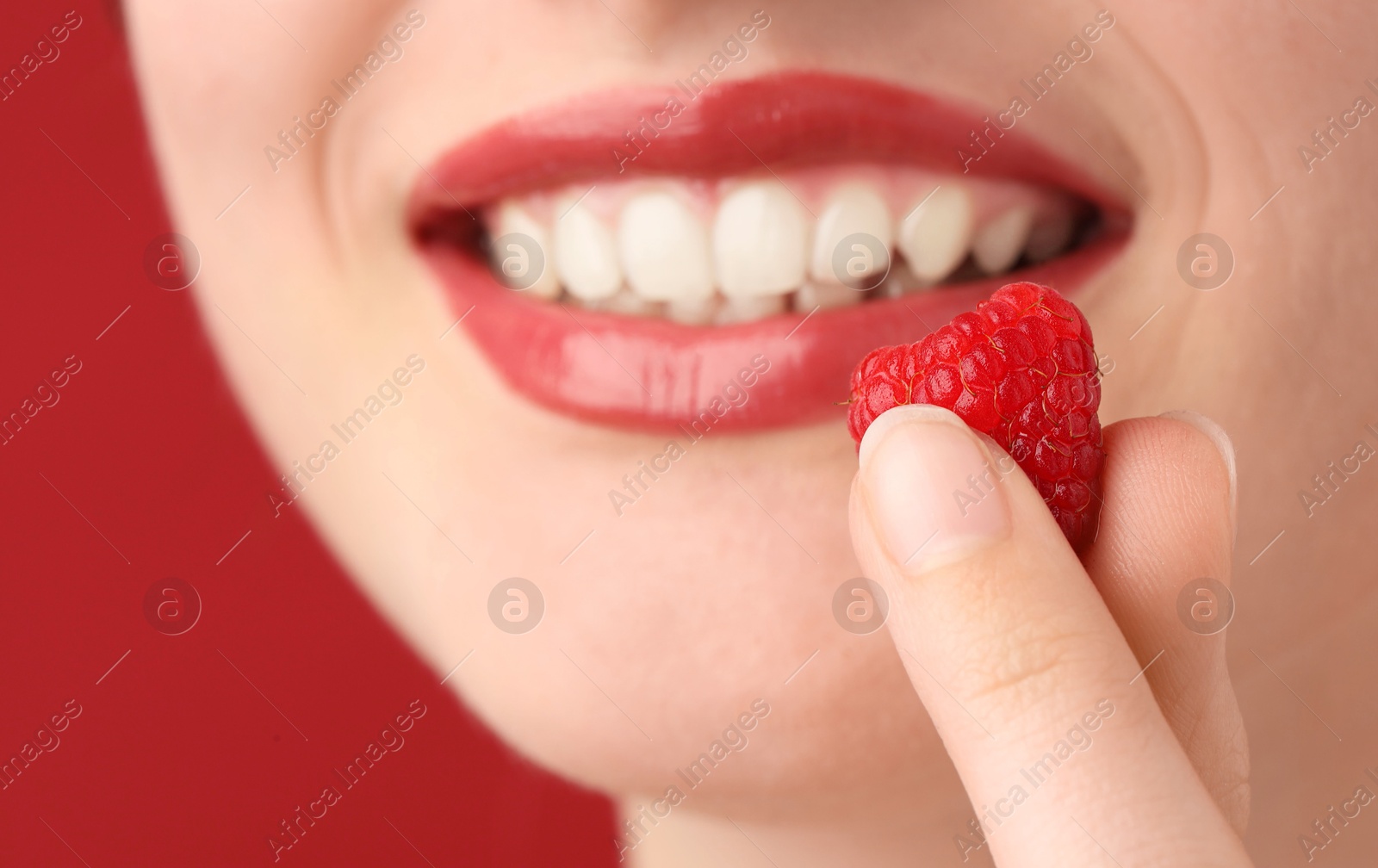 Photo of Woman with beautiful lips makeup and raspberry on red background, closeup
