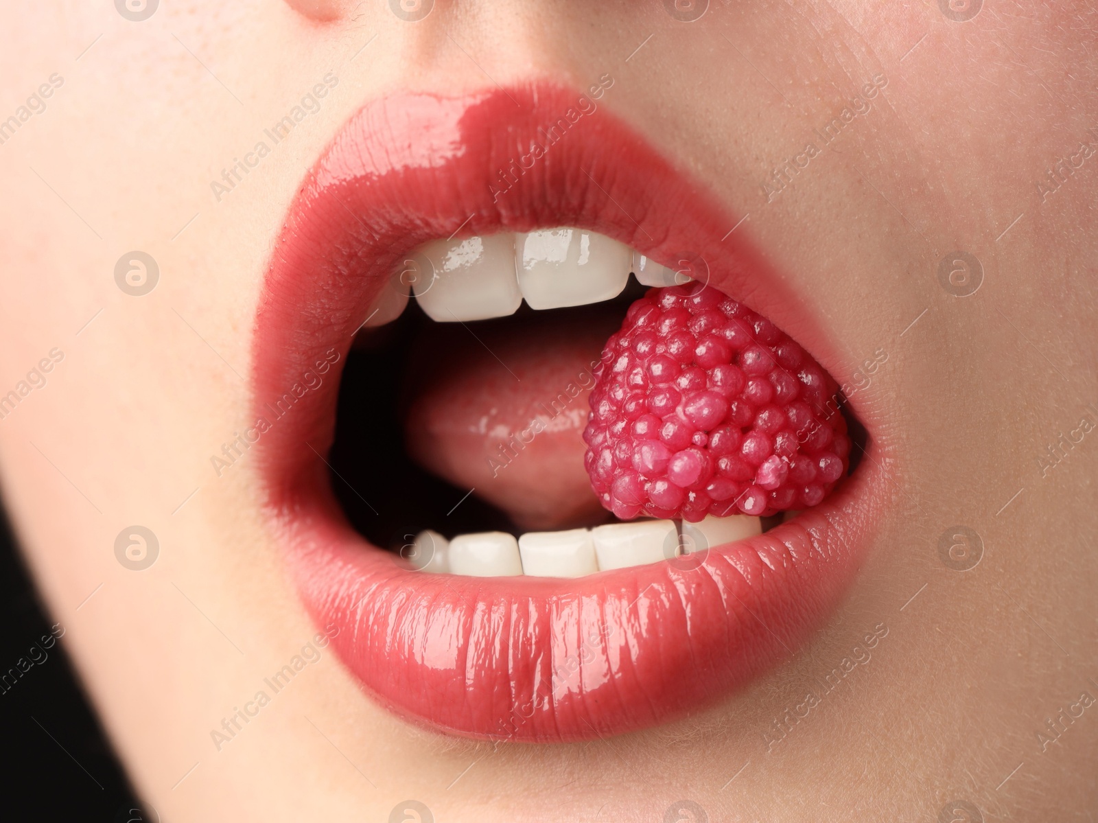 Photo of Woman with beautiful lips makeup and raspberry candy on black background, closeup