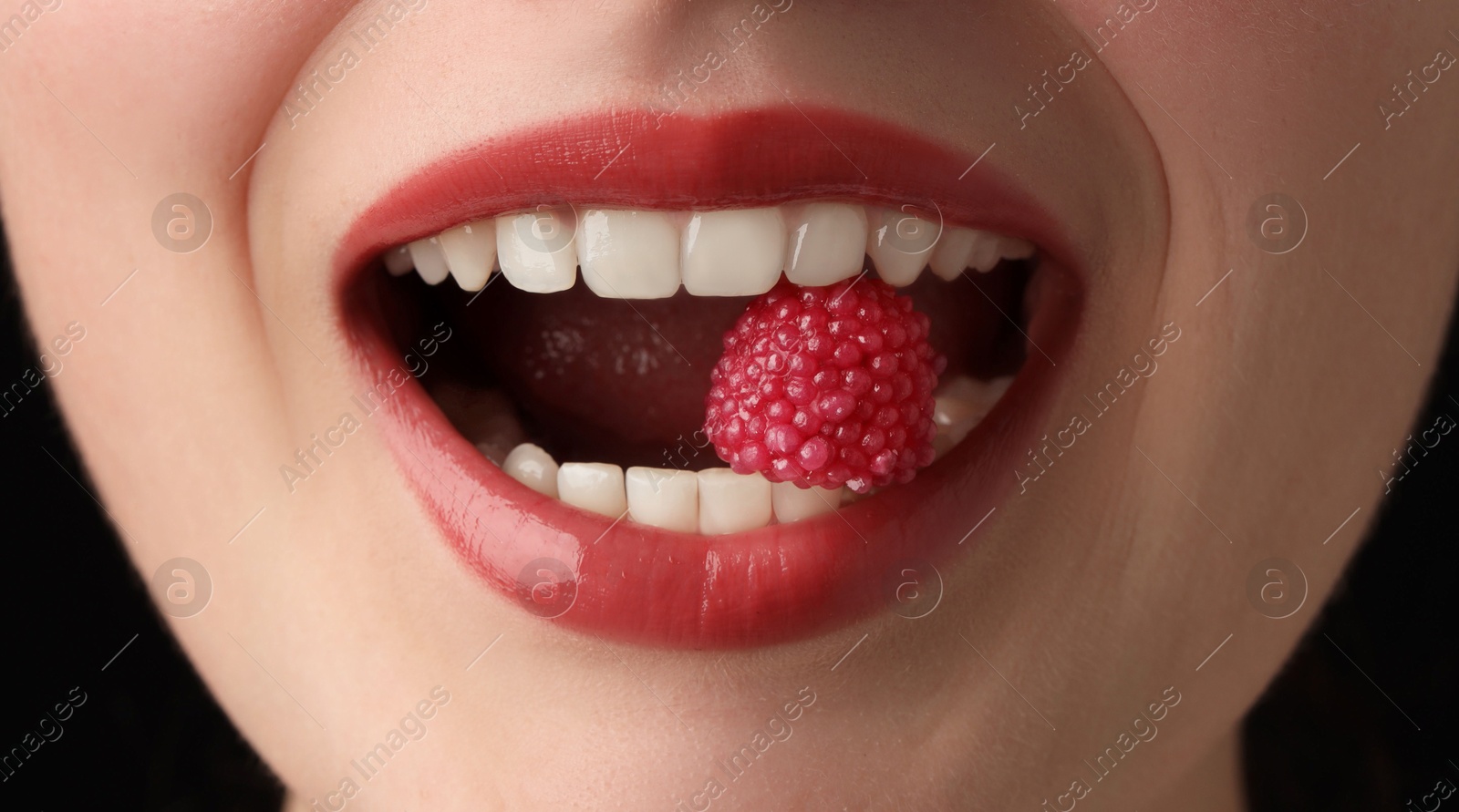 Photo of Woman with beautiful lips makeup and raspberry candy on black background, closeup