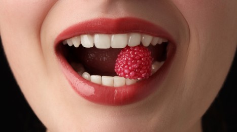 Photo of Woman with beautiful lips makeup and raspberry candy on black background, closeup