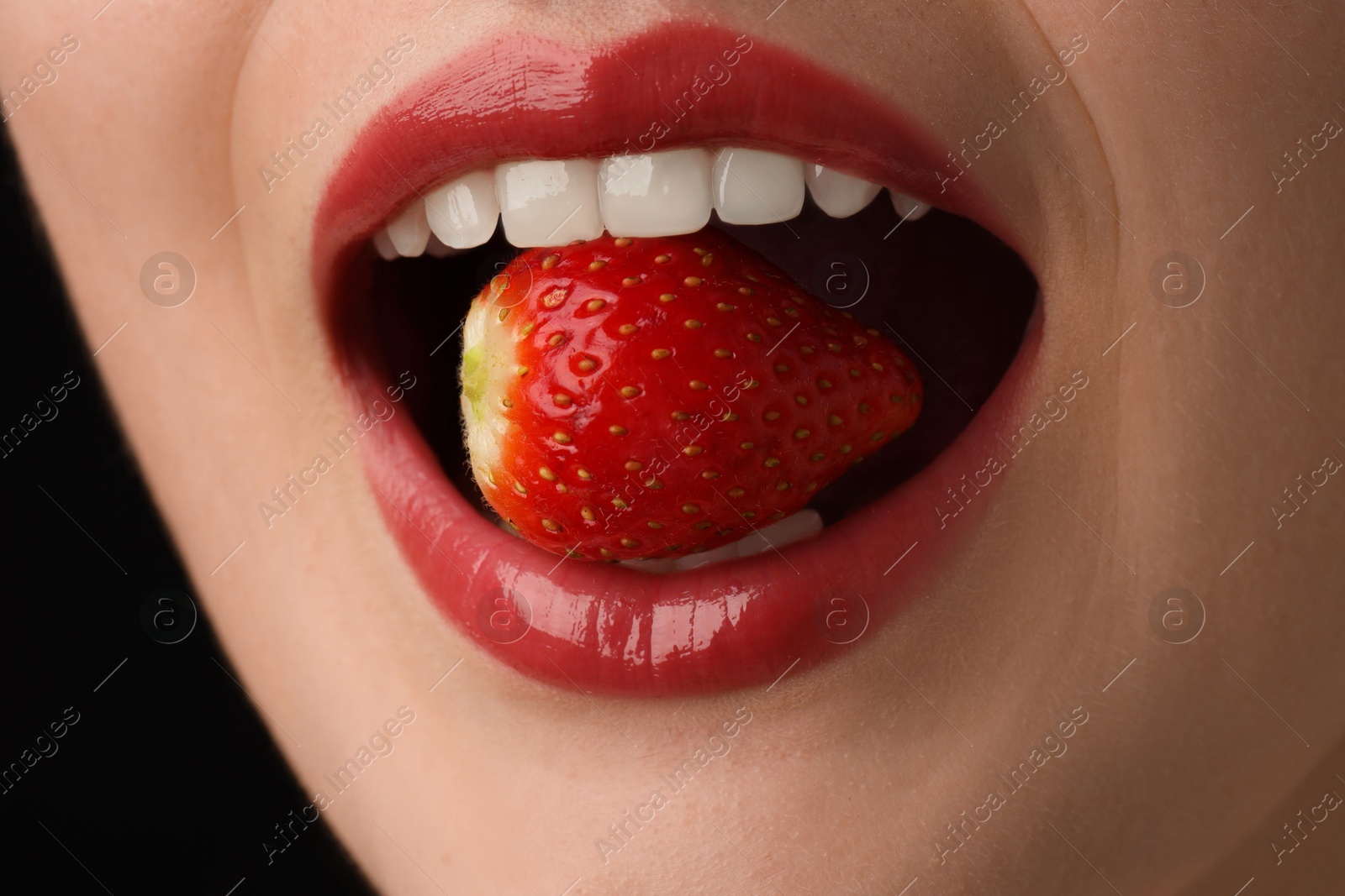 Photo of Woman with beautiful lips makeup and strawberry on black background, closeup