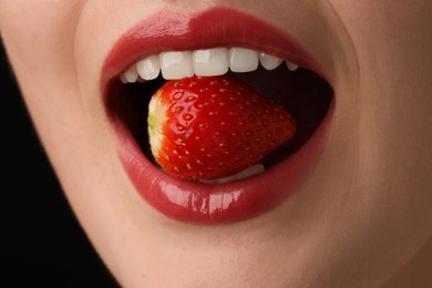 Photo of Woman with beautiful lips makeup and strawberry on black background, closeup