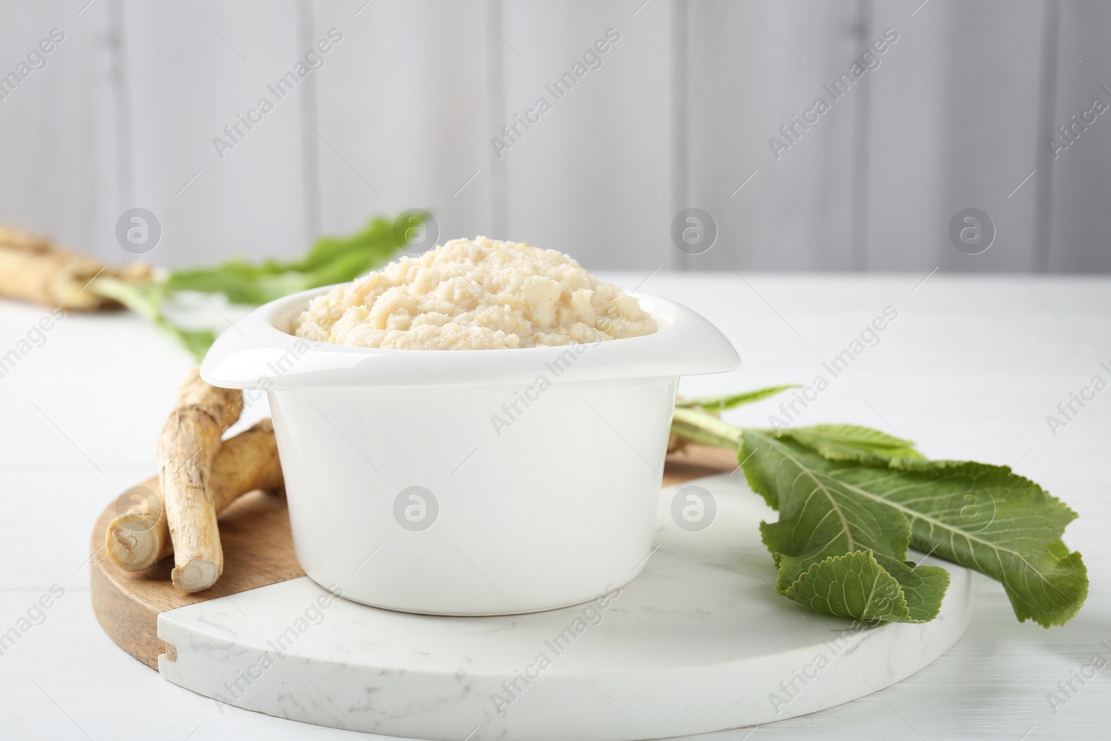 Photo of Tasty horseradish sauce and roots on white wooden table, closeup. Space for text