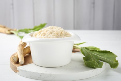 Photo of Tasty horseradish sauce and roots on white wooden table, closeup. Space for text