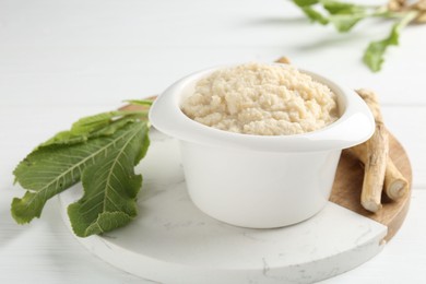 Photo of Tasty horseradish sauce and roots on white wooden table, closeup