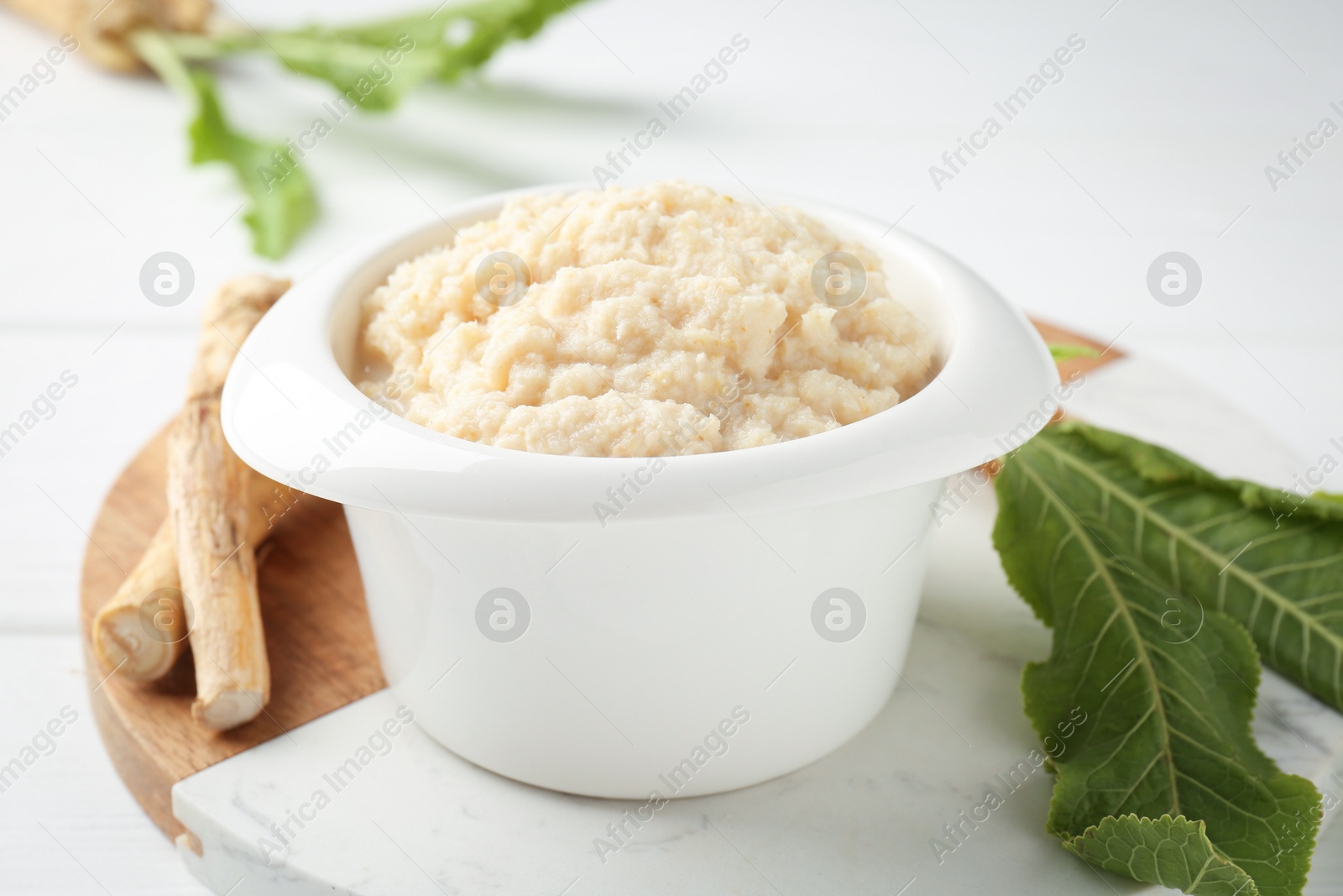 Photo of Tasty horseradish sauce and roots on white wooden table, closeup