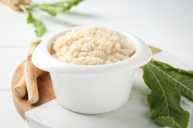 Photo of Tasty horseradish sauce and roots on white wooden table, closeup