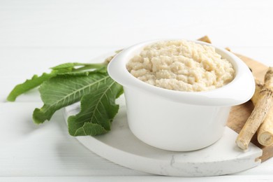 Photo of Tasty horseradish sauce and roots on white wooden table, closeup