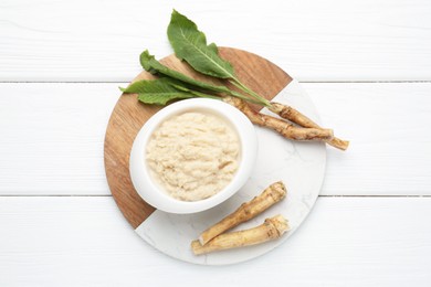 Photo of Tasty horseradish sauce and roots on white wooden table, top view