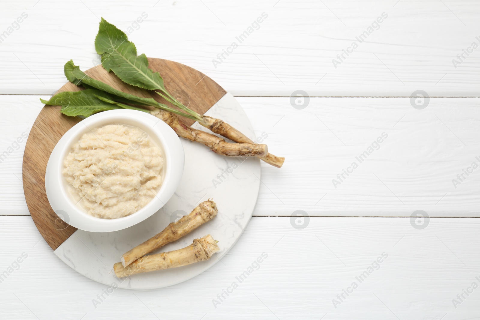 Photo of Tasty horseradish sauce and roots on white wooden table, top view. Space for text