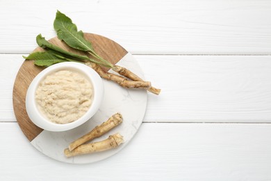 Photo of Tasty horseradish sauce and roots on white wooden table, top view. Space for text