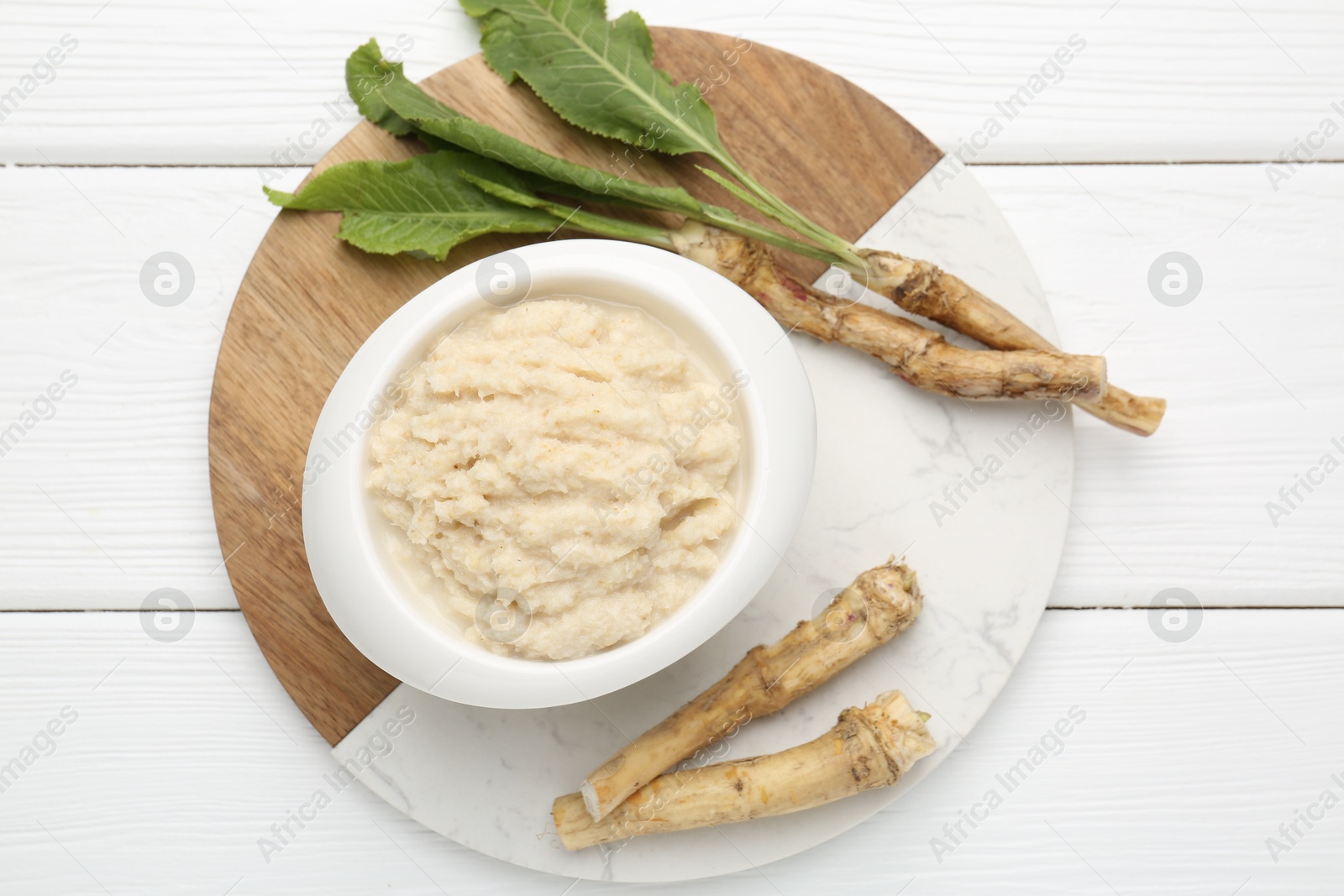 Photo of Tasty horseradish sauce and roots on white wooden table, top view