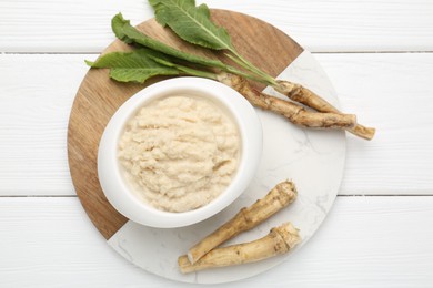 Photo of Tasty horseradish sauce and roots on white wooden table, top view