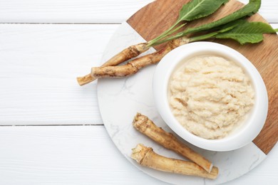 Photo of Tasty horseradish sauce and roots on white wooden table, top view