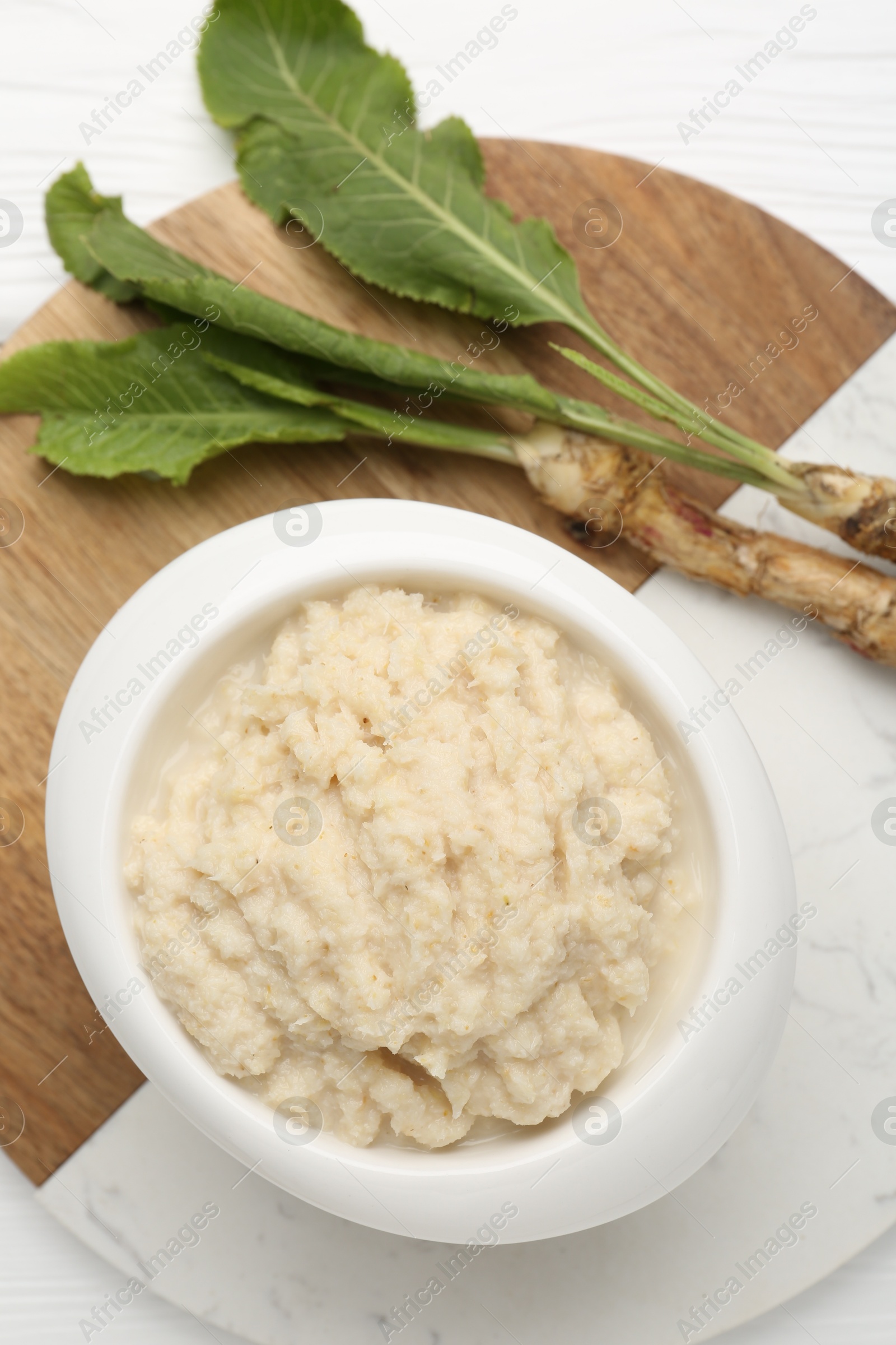 Photo of Tasty horseradish sauce and roots on white wooden table, top view
