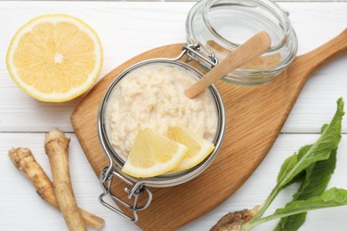 Photo of Tasty horseradish sauce with lemon slices and roots on white wooden table, flat lay