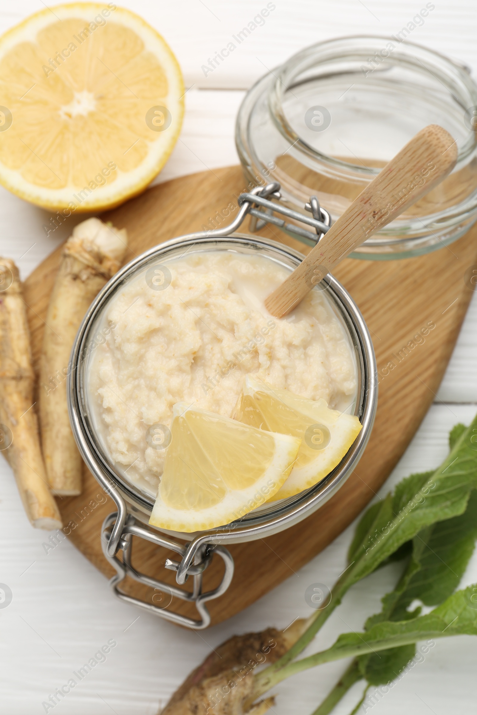 Photo of Tasty horseradish sauce with lemon slices and roots on white wooden table, flat lay