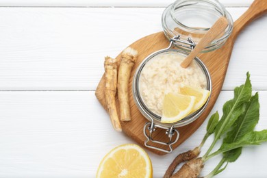 Photo of Tasty horseradish sauce with lemon slices and roots on white wooden table, flat lay. Space for text