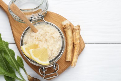 Photo of Tasty horseradish sauce with lemon slices and roots on white wooden table, flat lay