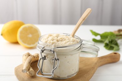 Photo of Tasty horseradish sauce, roots and lemons on white wooden table, closeup