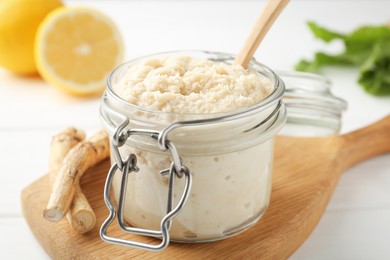 Photo of Tasty horseradish sauce, roots and lemons on white wooden table, closeup