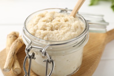 Photo of Tasty horseradish sauce and roots on white wooden table, closeup