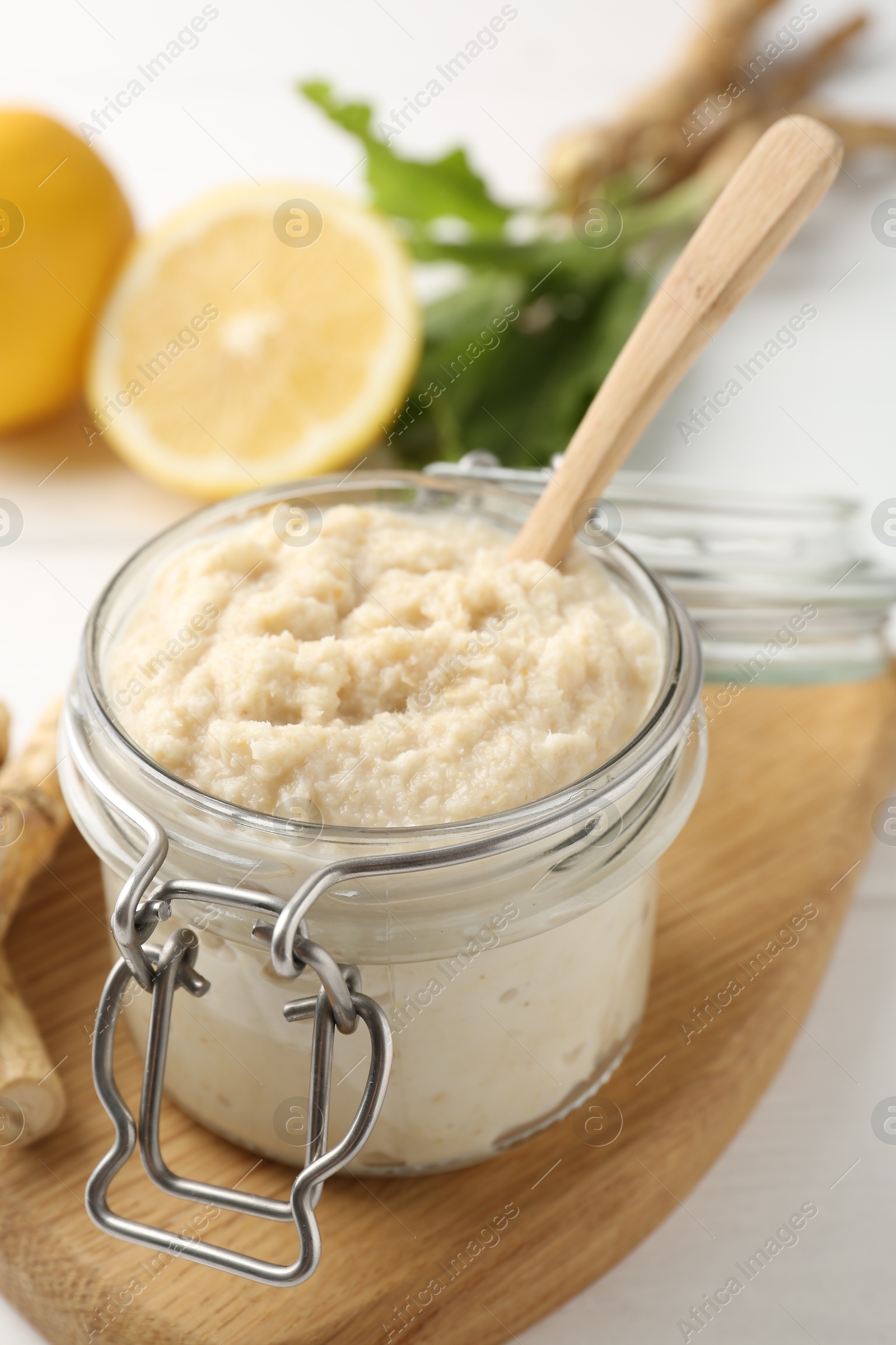 Photo of Tasty horseradish sauce, roots and lemons on white wooden table, closeup
