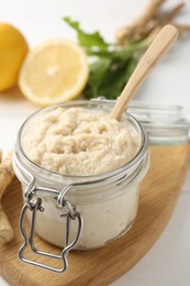 Photo of Tasty horseradish sauce, roots and lemons on white wooden table, closeup